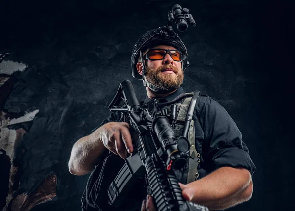 Soldato delle forze speciali che indossa giubbotti antiproiettile e casco con visione notturna con un fucile d'assalto. Studio foto contro un muro scuro strutturato — Foto Stock