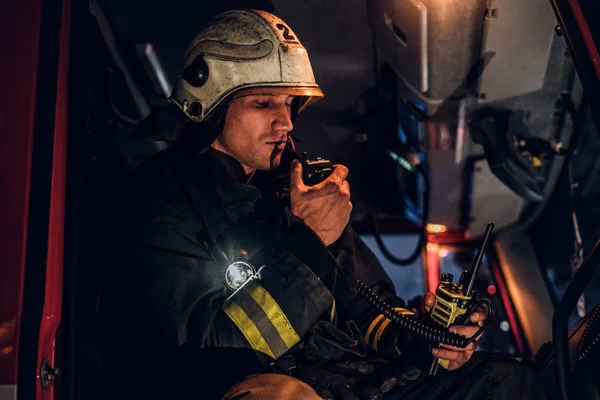 The fire brigade arrived at the night-time. Fireman sitting in the fire truck and talking on the radio — Stock Photo, Image