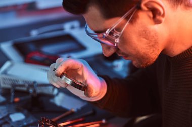 Elektronik teknisyeni kırık tablet dikkatli bir şekilde tamir çip bir büyüteç kullanarak Tablet inceliyor. Kırmızı ve Mavi ışıklı aydınlatma