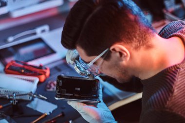 Teknisyen dikkatle smartphone içinde modern bir tamirciye iç unsurları bütünlüğünü inceler