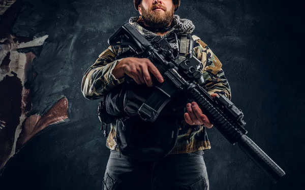 Special forces soldier in the military camouflaged uniform holding an assault rifle. Studio photo against a dark textured wall — Stock Photo, Image