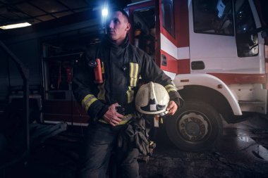 Tek tip bir kask tutarak ve yana doğru bir yangın kamyon bir itfaiye garajına yakın dururken seyir giyen itfaiyeci