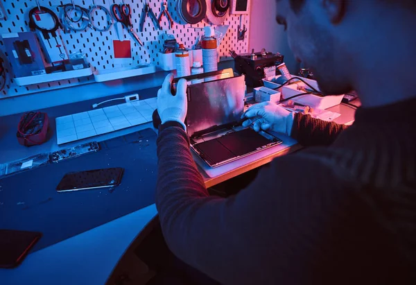 Der Techniker repariert einen kaputten Tablet-Computer in einer Werkstatt. Beleuchtung mit rotem und blauem Licht — Stockfoto