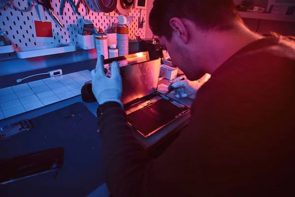 Der Techniker repariert einen kaputten Tablet-Computer in einer Werkstatt. Beleuchtung mit rotem und blauem Licht — Stockfoto