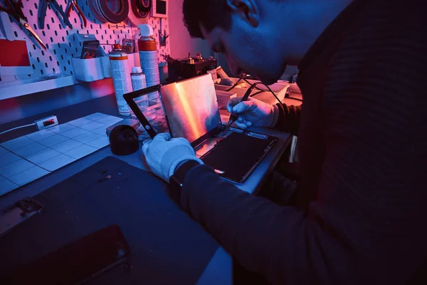 Der Techniker repariert einen kaputten Tablet-Computer in einer Werkstatt. Beleuchtung mit rotem und blauem Licht — Stockfoto