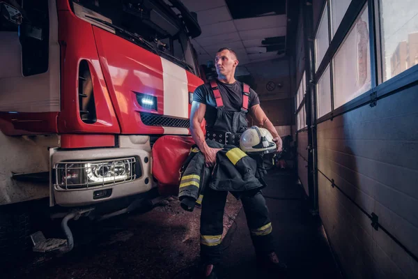 Bombero musculoso sosteniendo un casco protector en un garaje de un departamento de bomberos — Foto de Stock