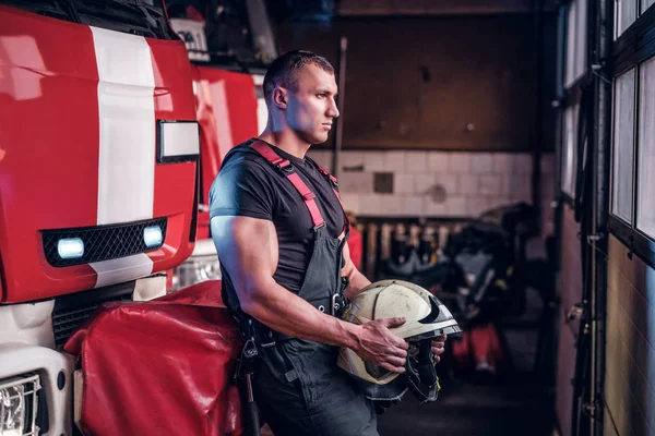 Svalnatý hasič držící ochrannou přilbu v garáži hasiči — Stock fotografie