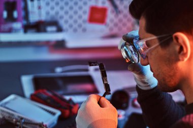 Elektronik teknisyeni kırık tablet dikkatli bir şekilde tamir çip bir büyüteç kullanarak Tablet inceliyor. Kırmızı ve Mavi ışıklı aydınlatma