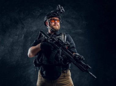 Özel Kuvvetler giyen çelik yelek ve kask ile gece görüş bir saldırı tüfeği tutan asker. Studio fotoğraf bir karanlık dokulu duvara