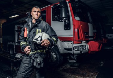 Tek tip bir kask tutarak ve yana doğru bir yangın kamyon bir itfaiye garajına yakın dururken seyir giyen itfaiyeci
