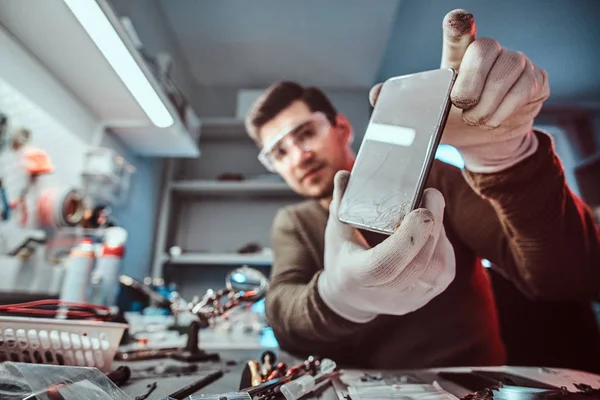 Técnico eletrônico mostrando um smartphone com um corpo quebrado em uma oficina — Fotografia de Stock