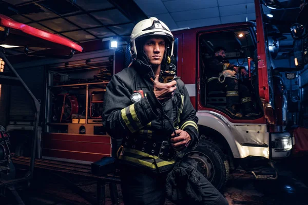 Fireman in a protective uniform standing next to a fire truck and talking on the radio. The fire brigade arrived at the night-time — Stock Photo, Image