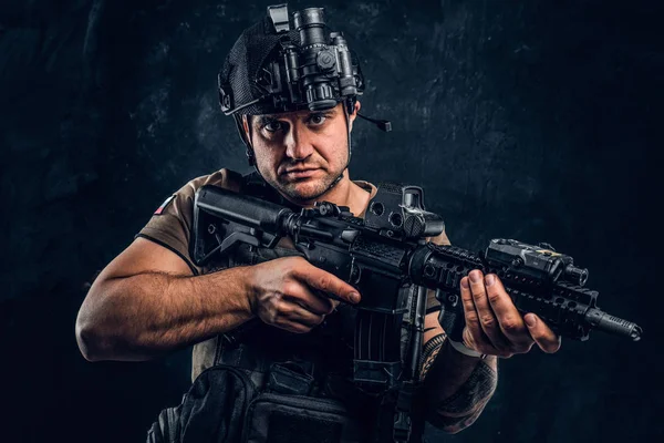 Soldado brutal en camiseta con tatuaje en la mano con chaleco antibalas y casco con una visión nocturna posando con un rifle de asalto . — Foto de Stock