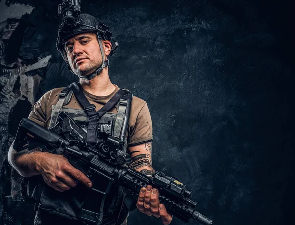 Brutaler Soldat im T-Shirt mit Tätowierung auf der Hand, der Körperpanzer trägt und Helm mit Nachtsichtgerät, der mit einem Sturmgewehr posiert. — Stockfoto