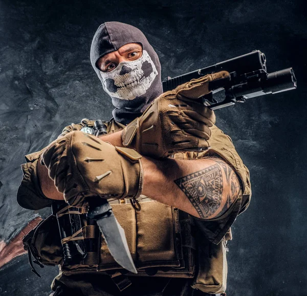 En terrorist i en militär uniform och en skalle balaclava håller en pistol och en kniv och ser på kameran med en hotfull blick — Stockfoto