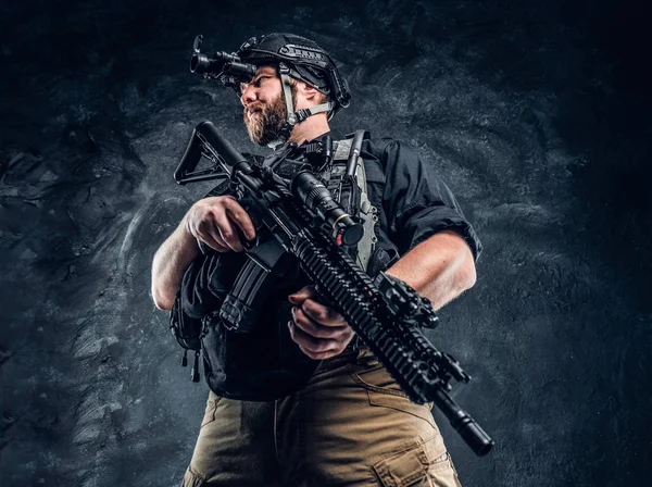 Bearded special forces soldier or private military contractor holding an assault rifle and observes the surroundings in night vision goggles. — Stock Photo, Image