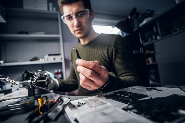 Elektroniker flickt ein kaputtes Telefon und betrachtet den kleinen Bolzen, der es mit einer Pinzette hält — Stockfoto