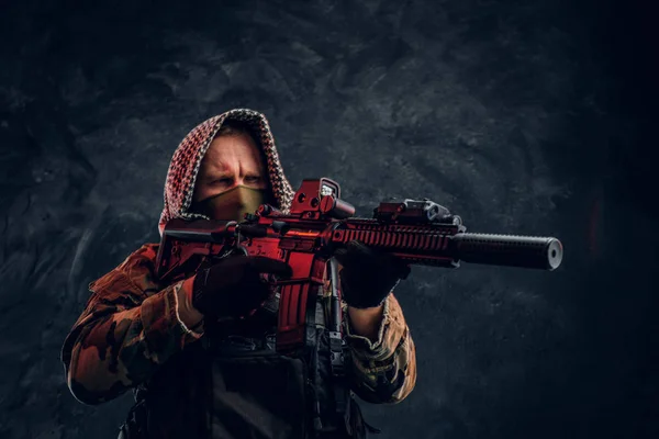Soldado de las fuerzas especiales en uniforme militar con máscara y capucha que sostiene un rifle de asalto con una mira láser y apunta al objetivo . — Foto de Stock