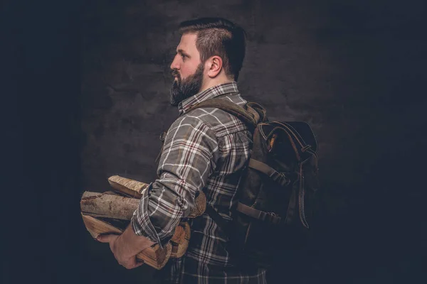 Портрет бородатого дровосека с рюкзаком в клетчатой рубашке с дровами . — стоковое фото