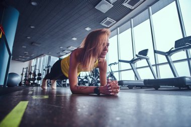 Modern spor salonunda, çalışma ince fitness kadının tahta bir mat yapması