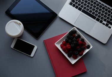 Ahududu, böğürtlen ve kahve, ofiste sağlıklı öğle yemeği. Dizüstü bilgisayar, tablet, smartphone ve defter bir tablo