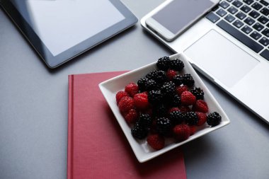 Dizüstü bilgisayar, tablet, smartphone ve defter bir tablo. Ahududu ve böğürtlen, ofiste sağlıklı Öğle Yemeği