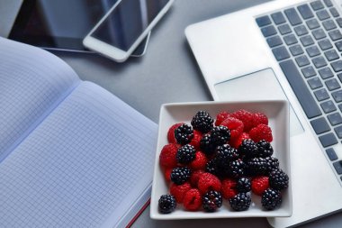 Dizüstü bilgisayar, tablet, smartphone ve defter bir tablo. Ahududu ve böğürtlen, ofiste sağlıklı Öğle Yemeği