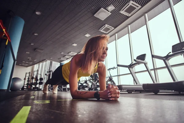 Mujer de fitness delgada que trabaja en el gimnasio moderno, haciendo la tabla en una estera — Foto de Stock