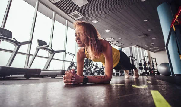 Schlanke Fitness-Frau, die im modernen Fitnessstudio arbeitet, beim Planken auf einer Matte — Stockfoto