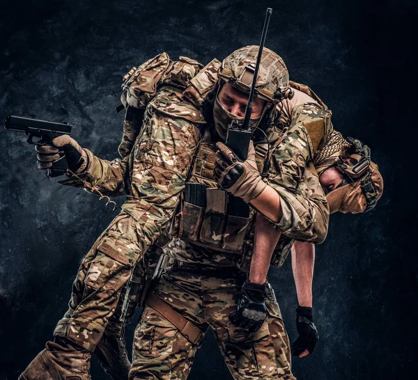 Soldaten-Spezialeinheiten retten seinen verwundeten Teamkollegen, der ihn auf seinen Schultern vom Schlachtfeld trägt, sprechen im Radio und rufen zur Unterstützung auf — Stockfoto