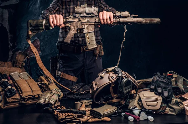 Hombre con camisa a cuadros sosteniendo un rifle de asalto y mostrando su uniforme militar y equipo. Equipo moderno de fuerzas especiales . — Foto de Stock