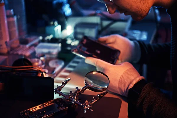Teknisyen dikkatle smartphone içinde modern bir tamirciye iç unsurları bütünlüğünü inceler