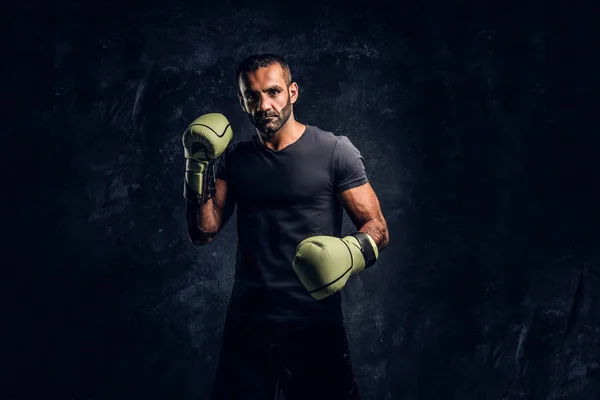 Porträtt av brutala professionell fighter i en svart tröja och handskar. Studio Foto mot en mörk texturerat vägg — Stockfoto