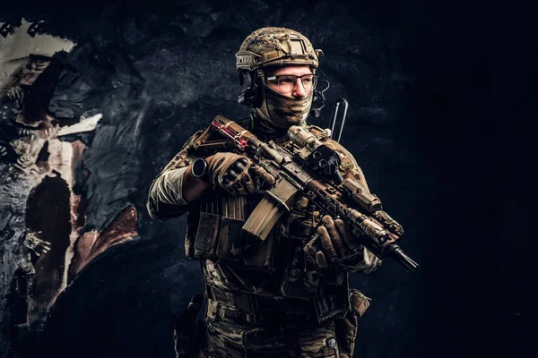 Soldado totalmente equipado con uniforme de camuflaje que sostiene un rifle de asalto. Foto del estudio contra una pared oscura — Foto de Stock