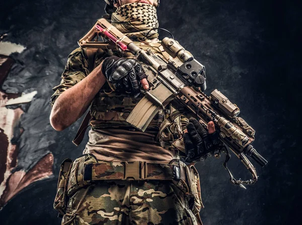 Soldado totalmente equipado con uniforme de camuflaje que sostiene un rifle de asalto. Foto del estudio contra una pared oscura — Foto de Stock