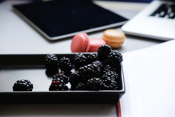 Bayas frescas y coloridos macarrones franceses. Ordenador portátil, tableta, teléfono inteligente y portátil en una mesa — Foto de Stock