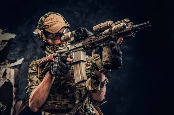 Fotografía del estudio de cerca contra una pared oscura. La unidad de élite, soldado de las fuerzas especiales en uniforme de camuflaje que sostiene un rifle de asalto con una mira láser y apunta a la targe —  Fotos de Stock