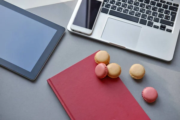 Laptop, tablet, smartphone, notebook and colorful French macaron on a table. Work, lunch, office — Stock Photo, Image