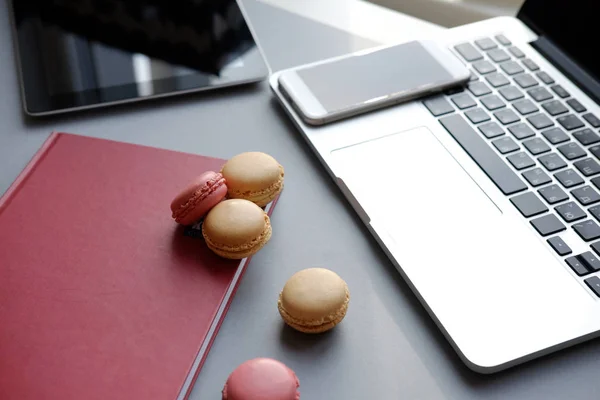 Laptop, tablet, smartphone, notebook y colorido macaron francés sobre una mesa. Trabajo, almuerzo, oficina — Foto de Stock
