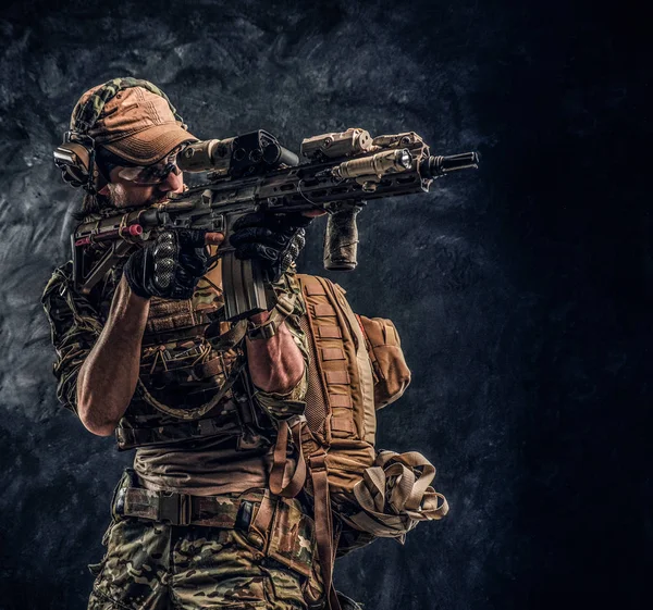 Die Eliteeinheit, ein Soldat der Spezialeinheiten in Tarnuniform, hält ein Sturmgewehr mit Laser-Visier in der Hand und zielt auf das Ziel. Studiofoto vor dunkler Wand — Stockfoto