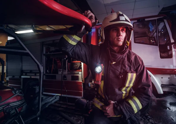 Portrait of a handsome fireman wearing a protective uniform with flashlight included standing in a fire station garage