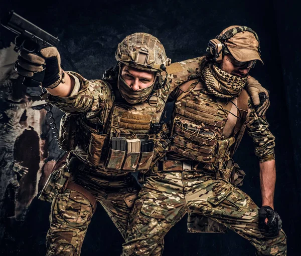 Conflicto de combate, misión especial. El soldado militar llevando a su compañero de equipo fuera del campo de batalla. Foto del estudio contra una pared oscura — Foto de Stock