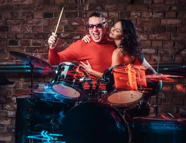 Mädchen umarmt ihr Idol, das auf einem Schlagzeug in einem Nachtclub gegen eine Ziegelwand spielt — Stockfoto