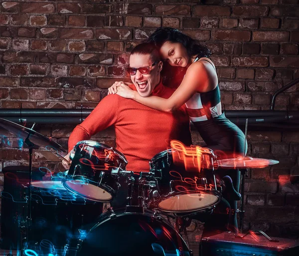 Girl hugs her idol who plays on a drum set in nightclub against a brick wall — Stock Photo, Image