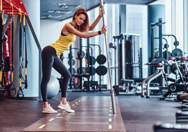 Modern spor salonunda bir halter üzerine eğilerek bir kamera için poz fitness kız — Stok fotoğraf