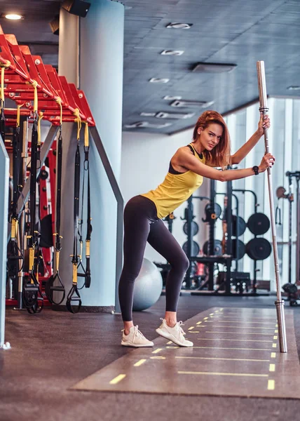 Modern spor salonunda bir halter üzerine eğilerek bir kamera için poz fitness kız — Stok fotoğraf