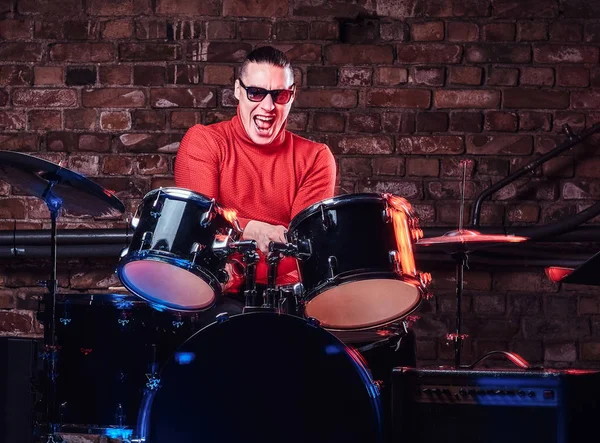 Stijlvolle musicus in zonnebril emotioneel drummen tegen bakstenen muur achtergrond — Stockfoto