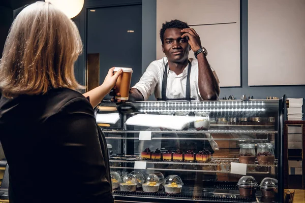 African barista gives the ordered coffee customer of modern coffee shop