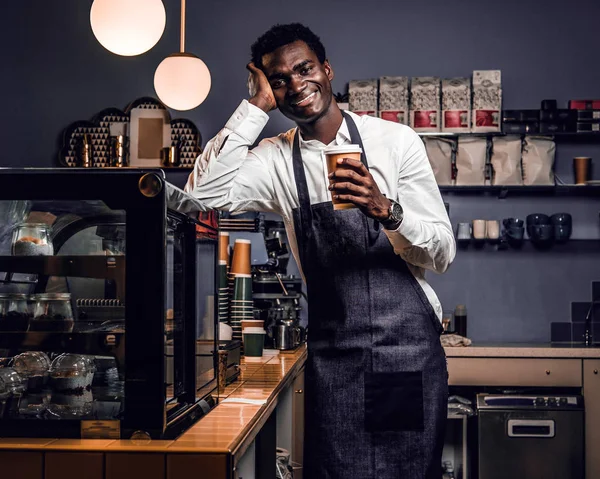 Bir fincan kahve ile bir kafede bir sayaçta yaslanmış ve mutlu bir bakışla bir kameraya bakarak süre tutarak yorgun barista 