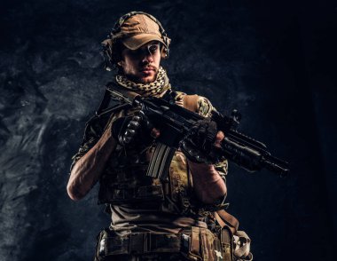 Asker kamuflaj bir saldırı tüfeği tutan tek tip içinde tam donanımlı. Karanlık bir duvara Studio fotoğraf